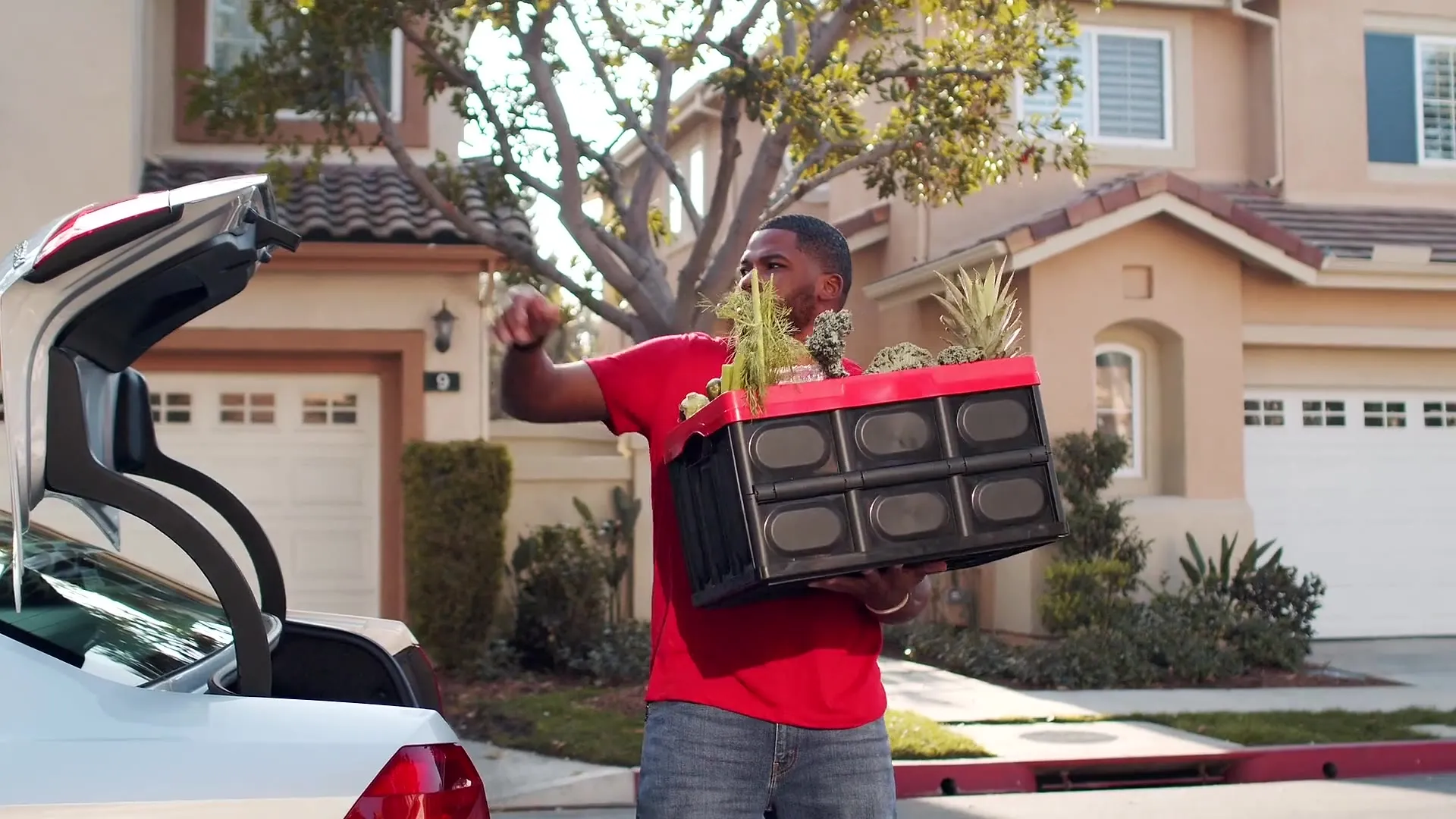 Delivery driver lifting a crate of groceries out of his car trunk