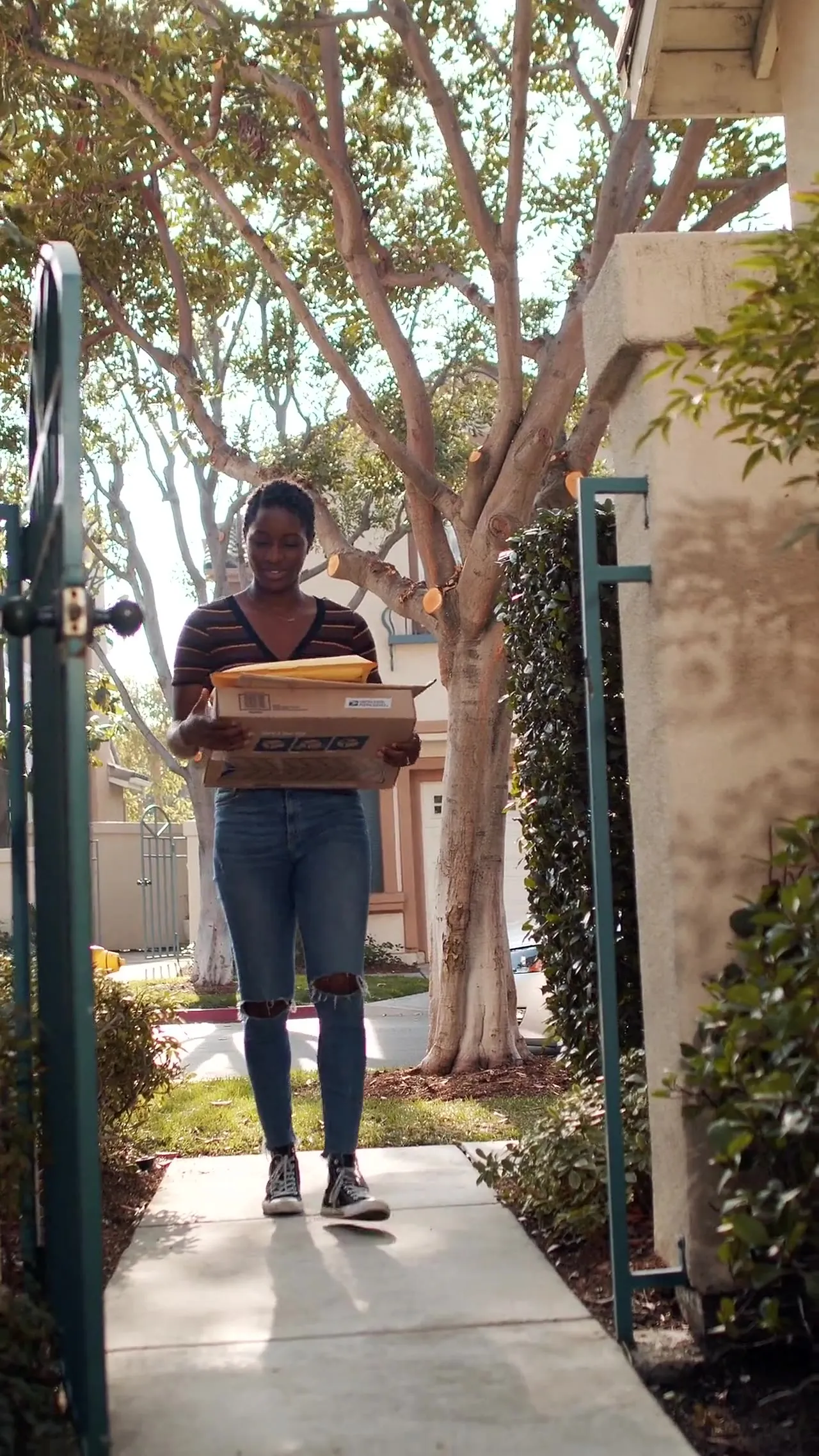 Smiling courier carrying packages through a garden gate